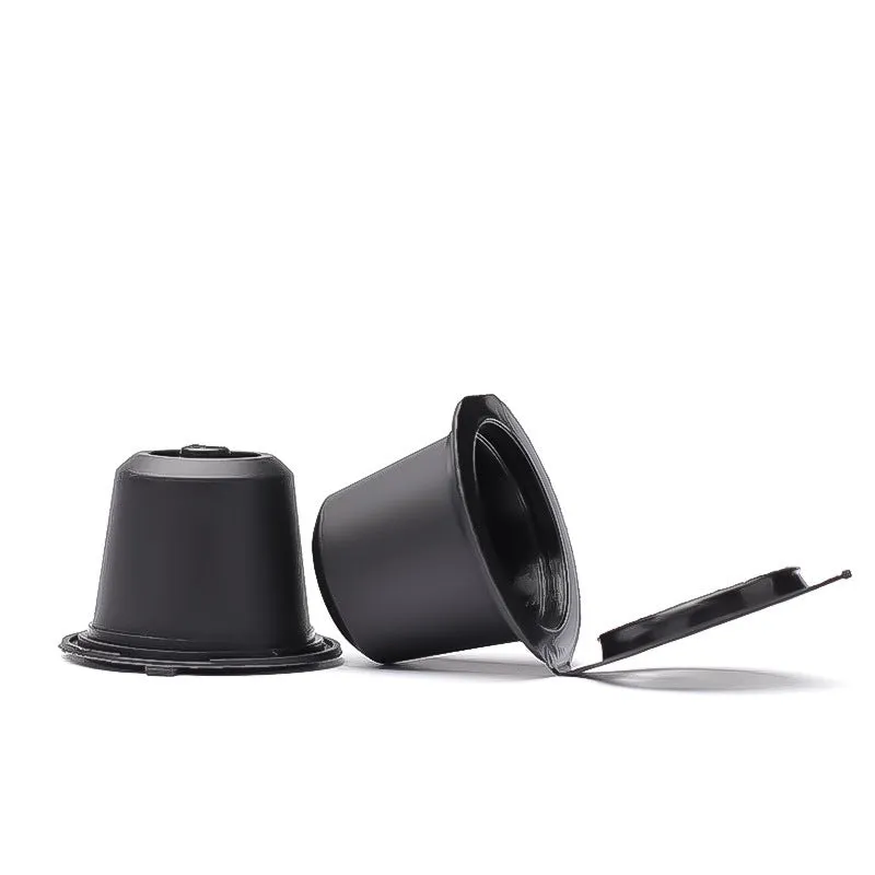 Six reusable black plastic coffee capsule filter cups with a spoon on a table