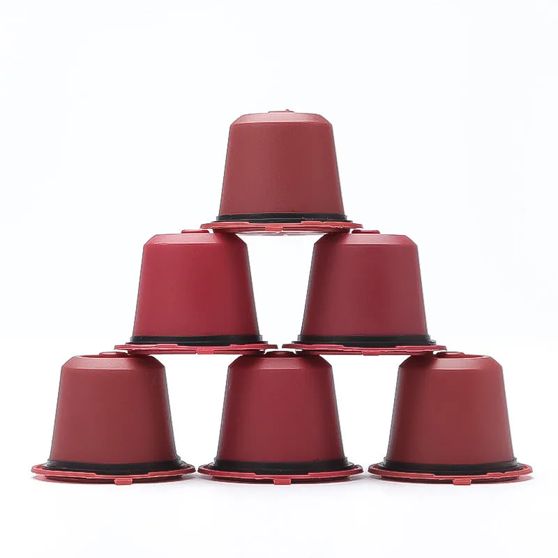 Six reusable black plastic coffee capsule filter cups with a spoon on a table