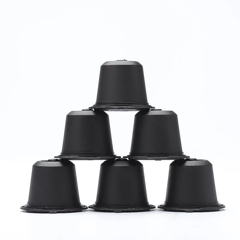 Six reusable black plastic coffee capsule filter cups with a spoon on a table