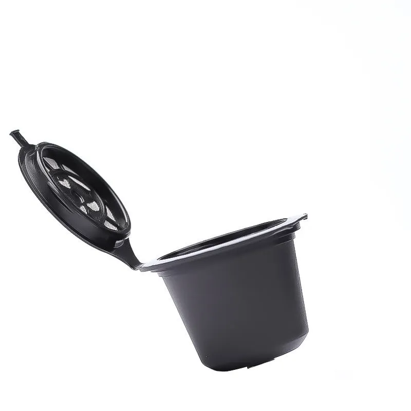 Six reusable black plastic coffee capsule filter cups with a spoon on a table
