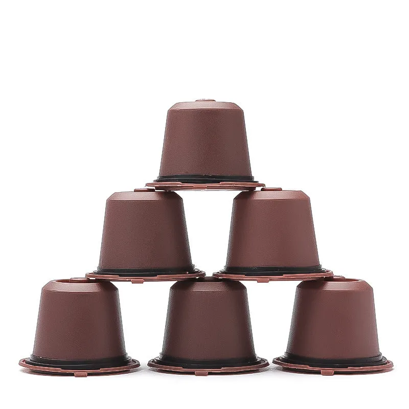 Six reusable black plastic coffee capsule filter cups with a spoon on a table