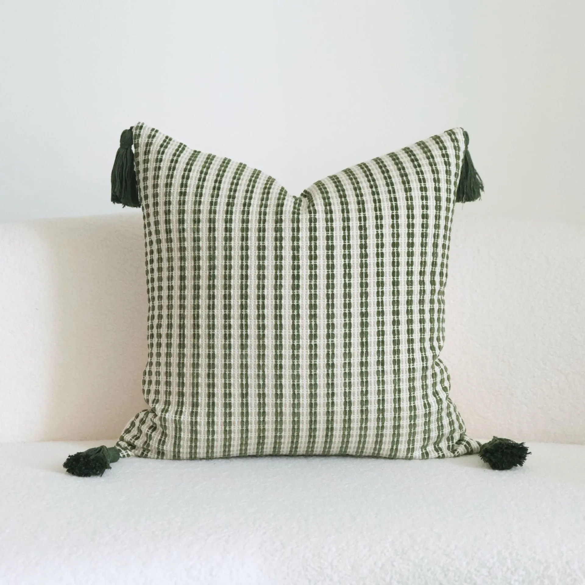 Green cotton and linen hotel sample pillow with botanical pattern and tassel detail on a display bed.