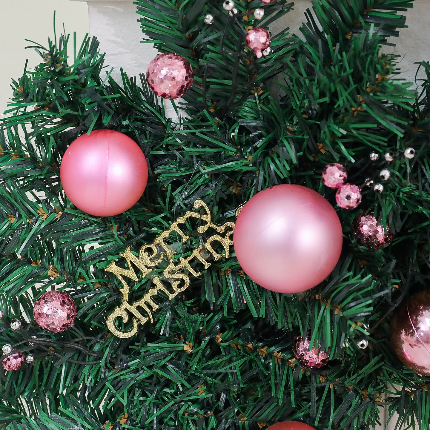 Pink artificial Christmas rattan vine decoration with small fruit clusters and warm white LED lights, coiled on a table.