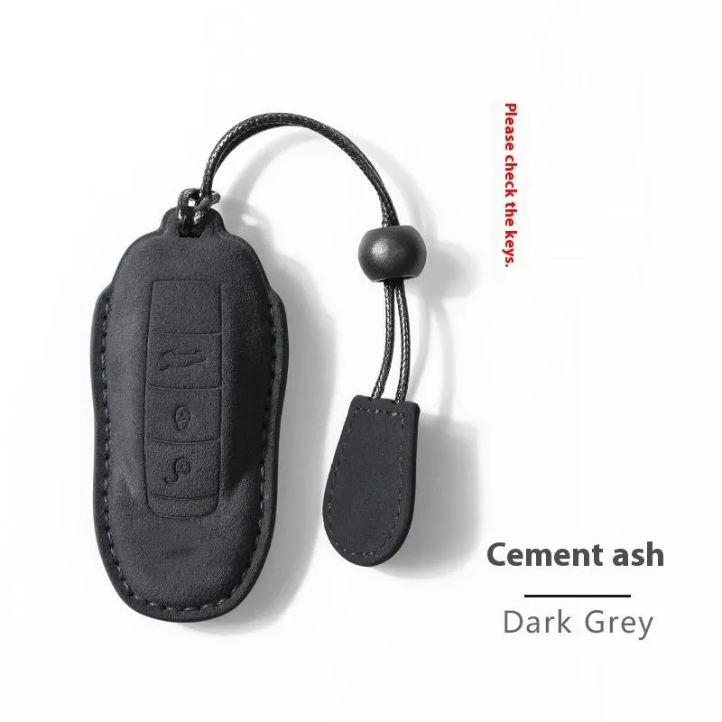 Suede car key cover in cement grey, dark green, light grey, and orange colour options on a plain background.