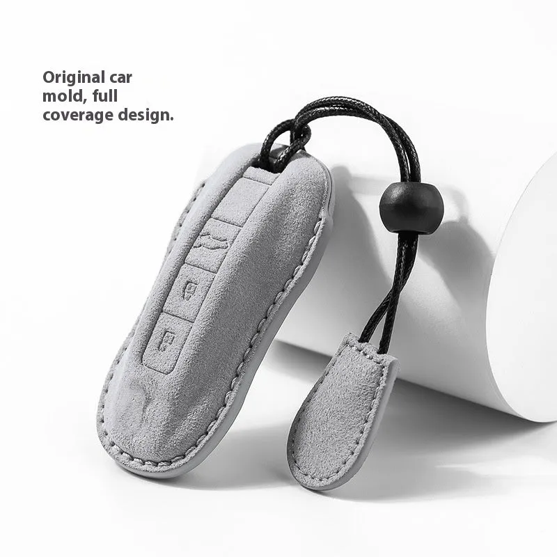 Suede car key cover in cement grey, dark green, light grey, and orange colour options on a plain background.