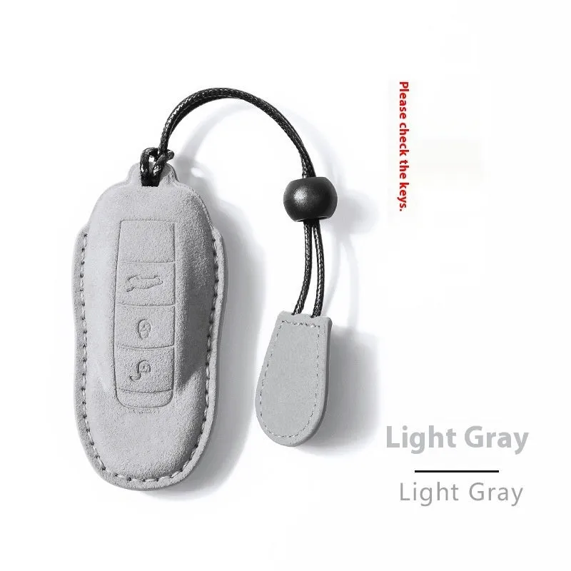 Suede car key cover in cement grey, dark green, light grey, and orange colour options on a plain background.