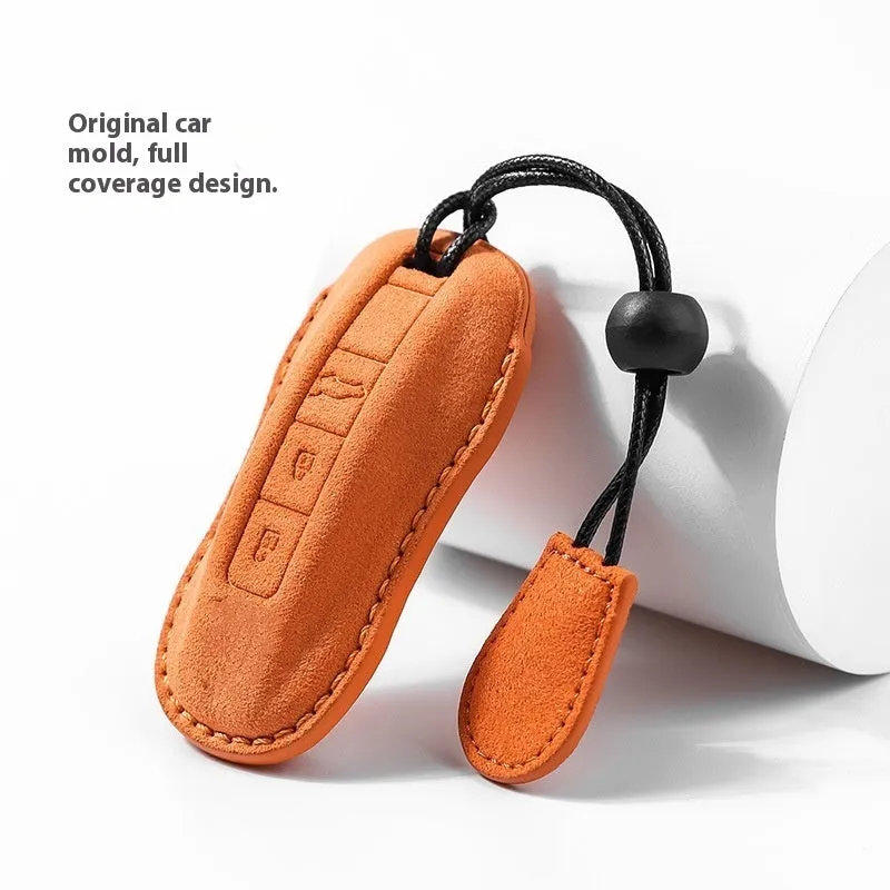 Suede car key cover in cement grey, dark green, light grey, and orange colour options on a plain background.