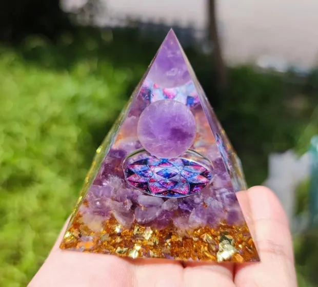 Small 6cm high clear epoxy resin pyramid ornament filled with colourful natural crystal gravel on a shelf.