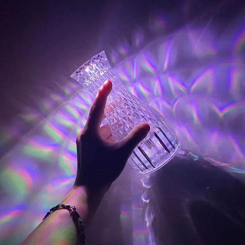 Vase-shaped transparent crystal bedside lamp with touch controls and LED lights on a table.