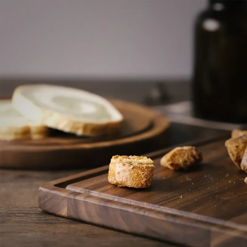 Solid black walnut wood chopping board with a deep perimeter groove and a side handle, shown as a serving tray.