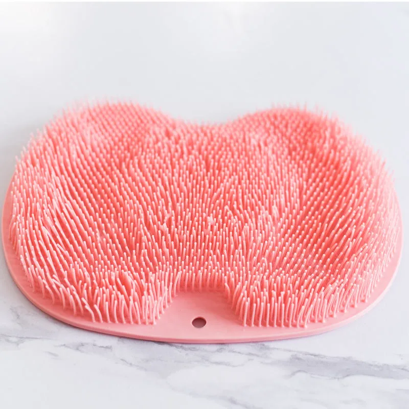 Orange non-slip massage bath brush with suction cups and soft silicone bristles on a bathroom floor.