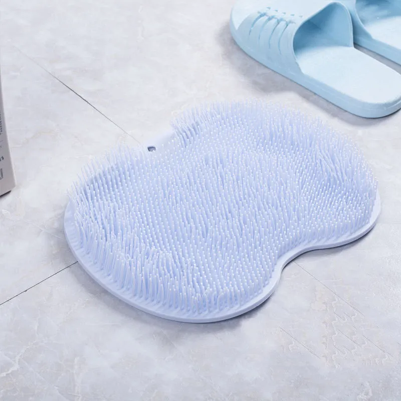 Orange non-slip massage bath brush with suction cups and soft silicone bristles on a bathroom floor.
