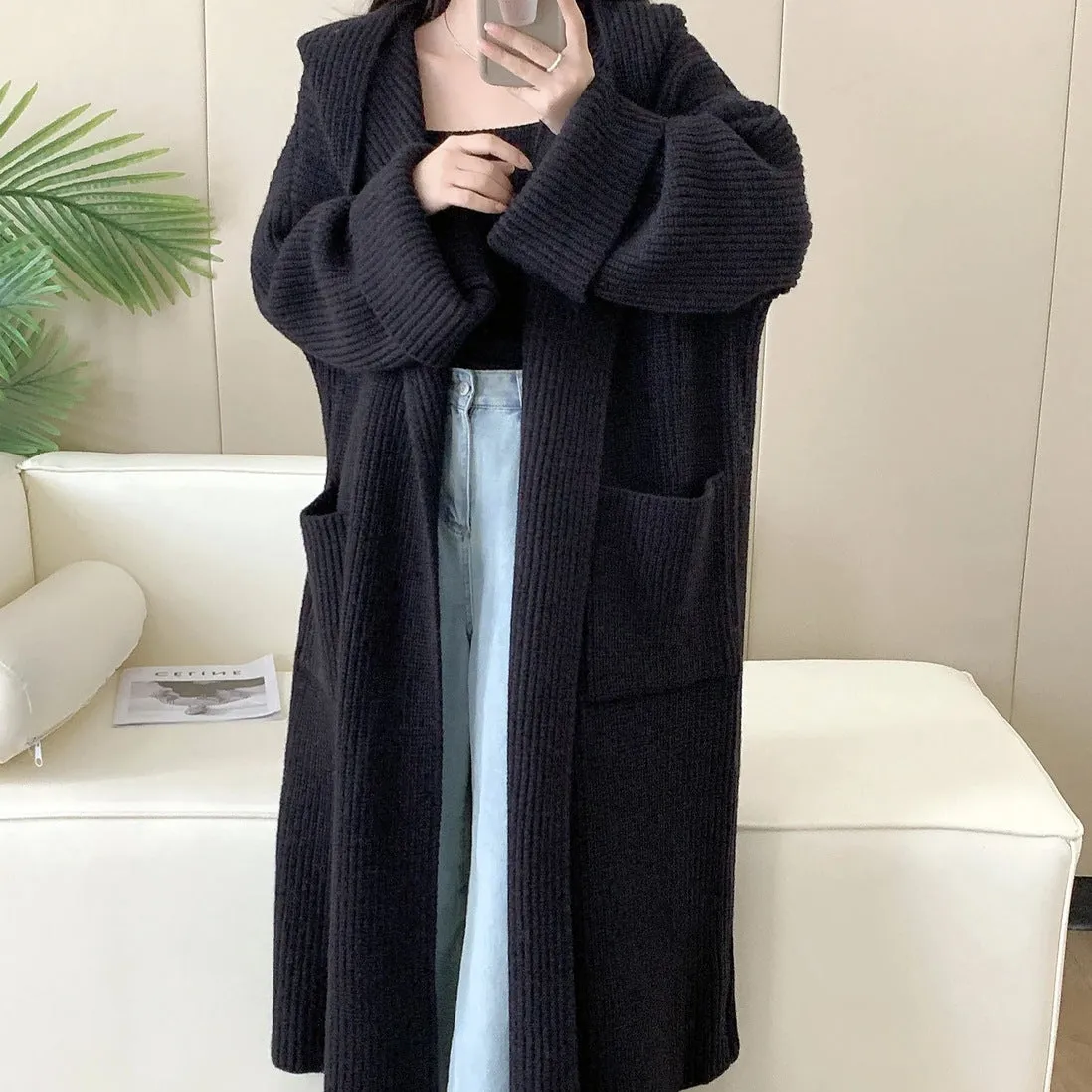 A woman wearing a long, loose, hooded cardigan coat in a neutral colour, showing its oversized fit and length.