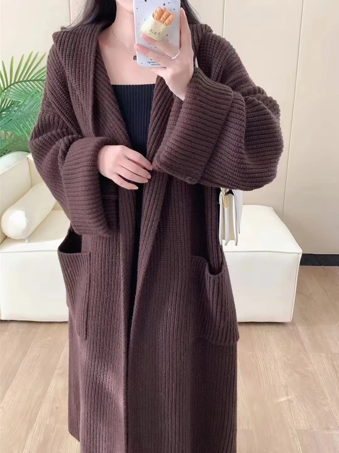 A woman wearing a long, loose, hooded cardigan coat in a neutral colour, showing its oversized fit and length.