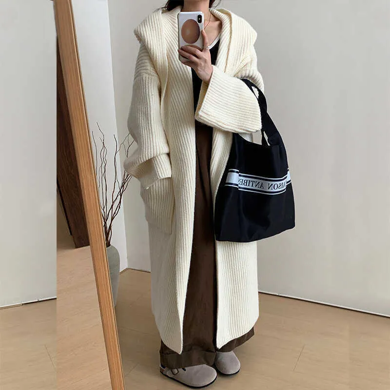 A woman wearing a long, loose, hooded cardigan coat in a neutral colour, showing its oversized fit and length.
