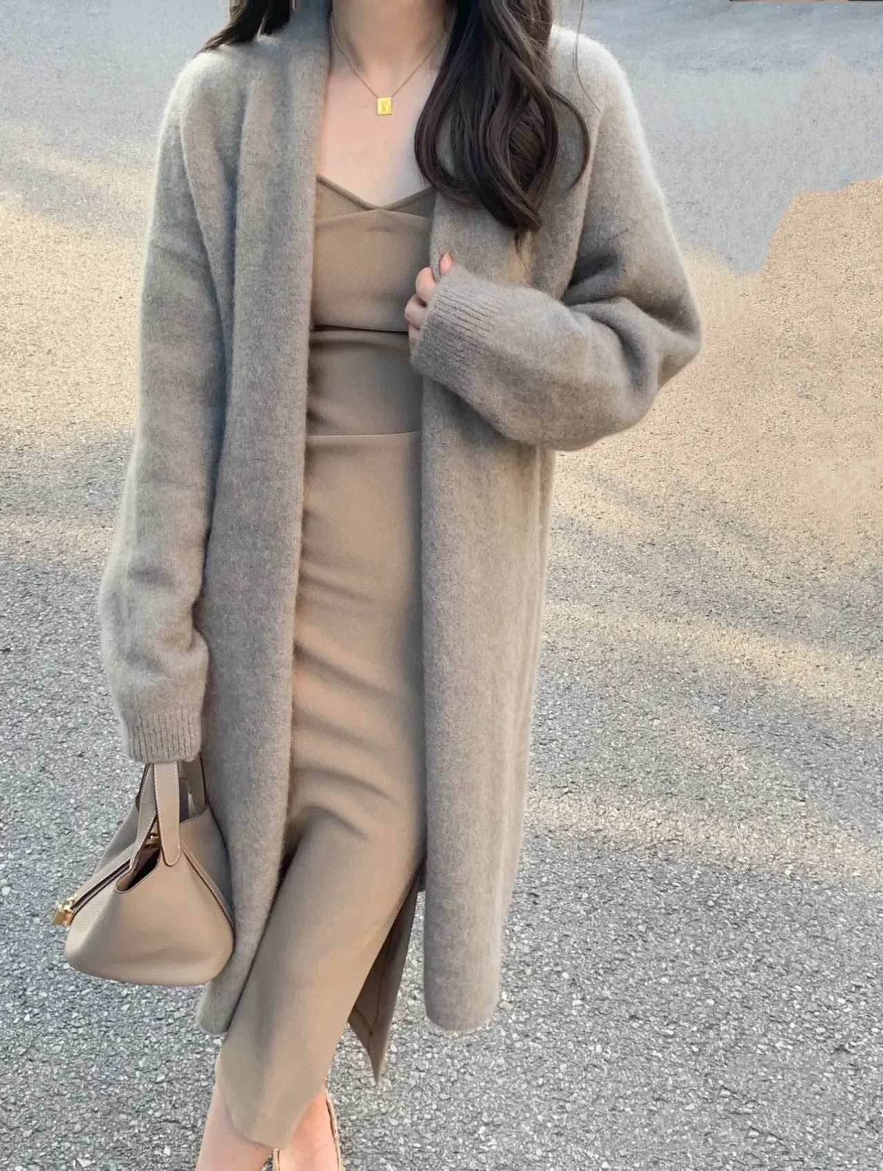A woman's loose-fit knitted cardigan in a khaki colour with a V-neck and long sleeves, laid flat.