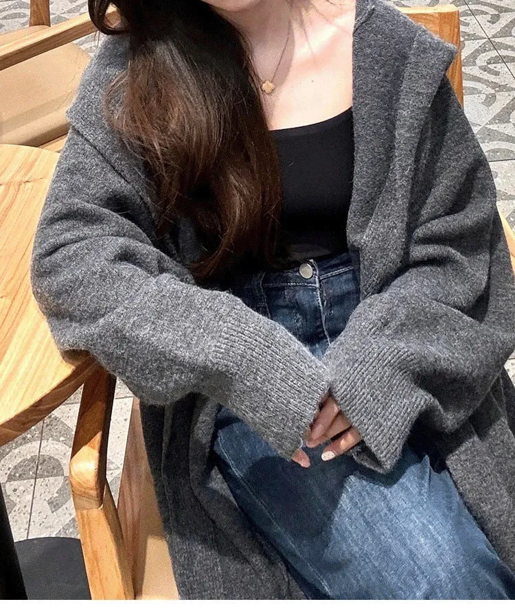 A woman wearing a long, loose, beige hooded knitted cardigan in a Korean casual style.