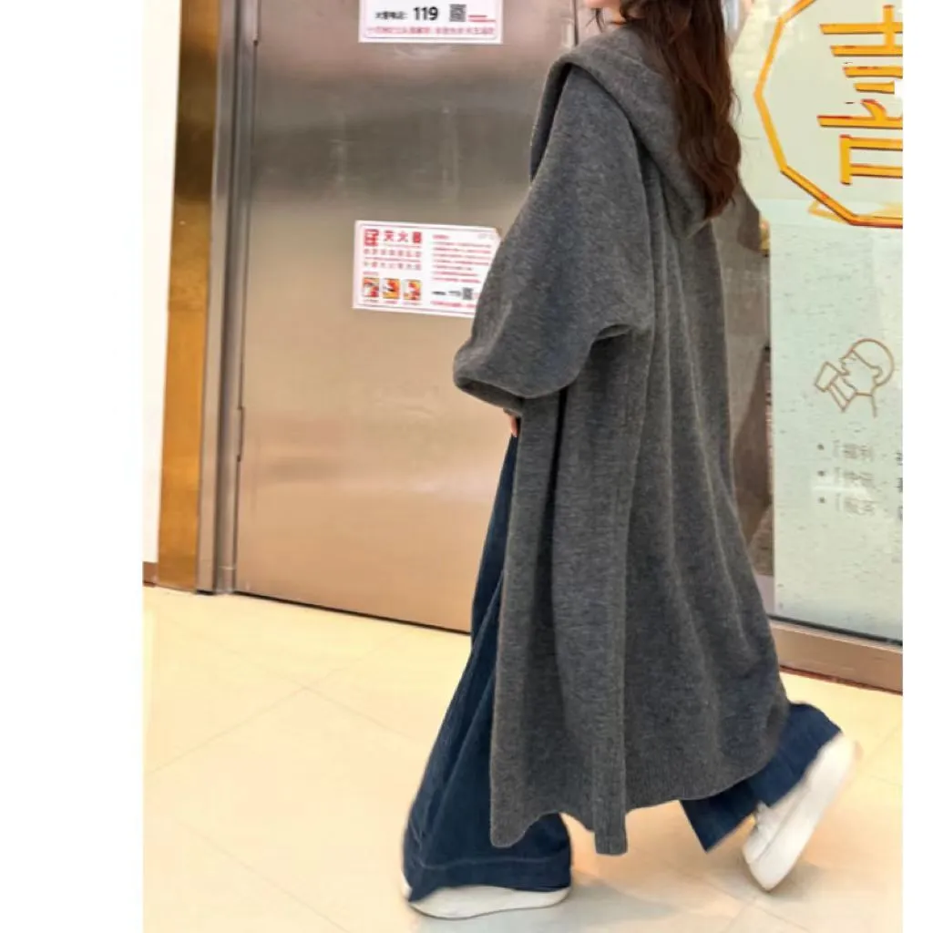 A woman wearing a long, loose, beige hooded knitted cardigan in a Korean casual style.