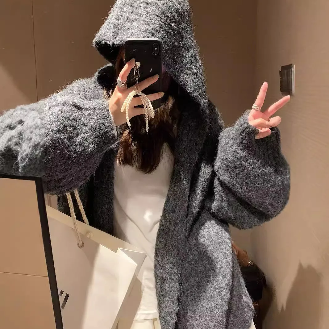A woman wearing a thick, loose-fit, dark grey hooded sweater cardigan with a retro design.