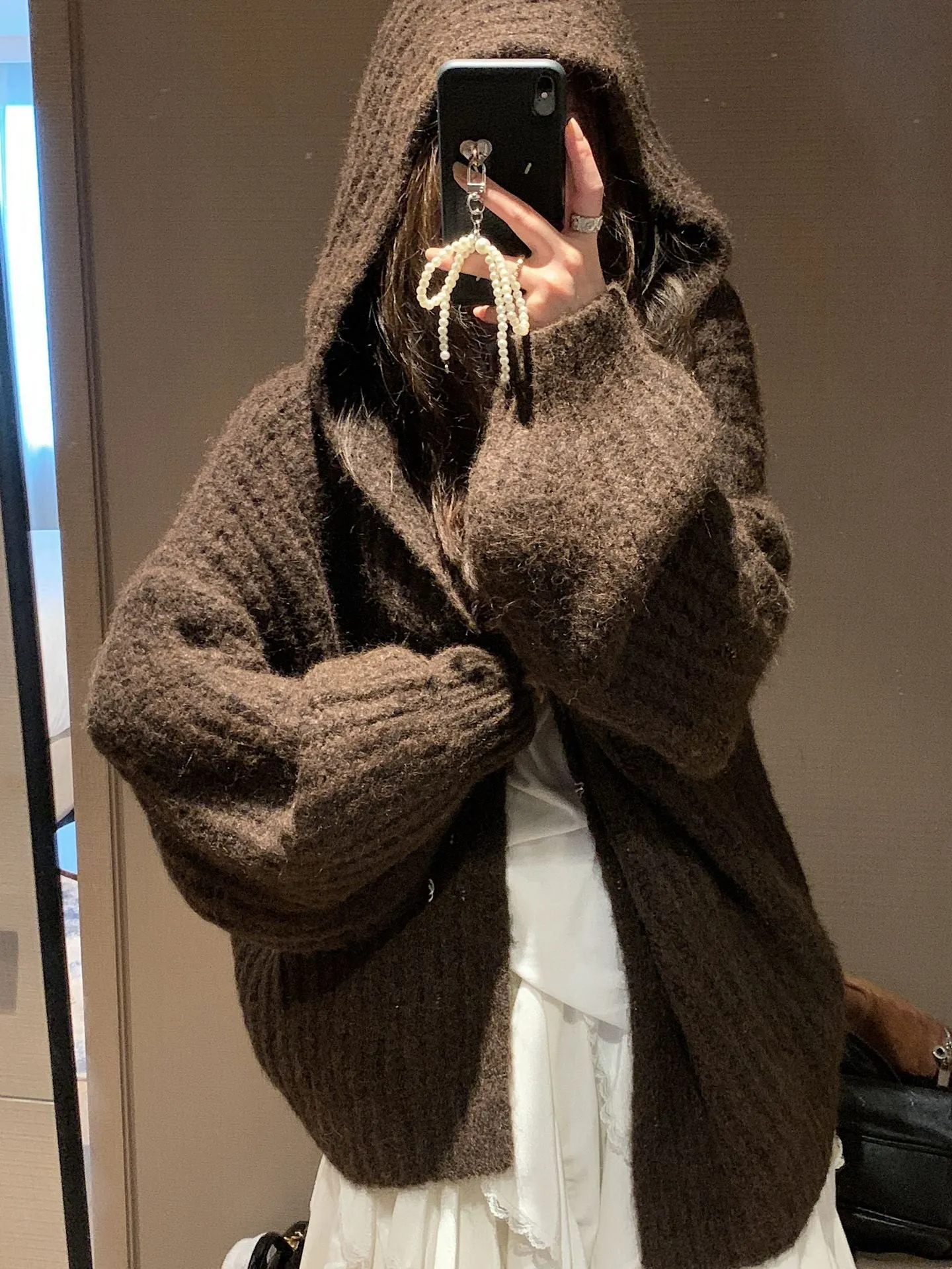 A woman wearing a thick, loose-fit, dark grey hooded sweater cardigan with a retro design.