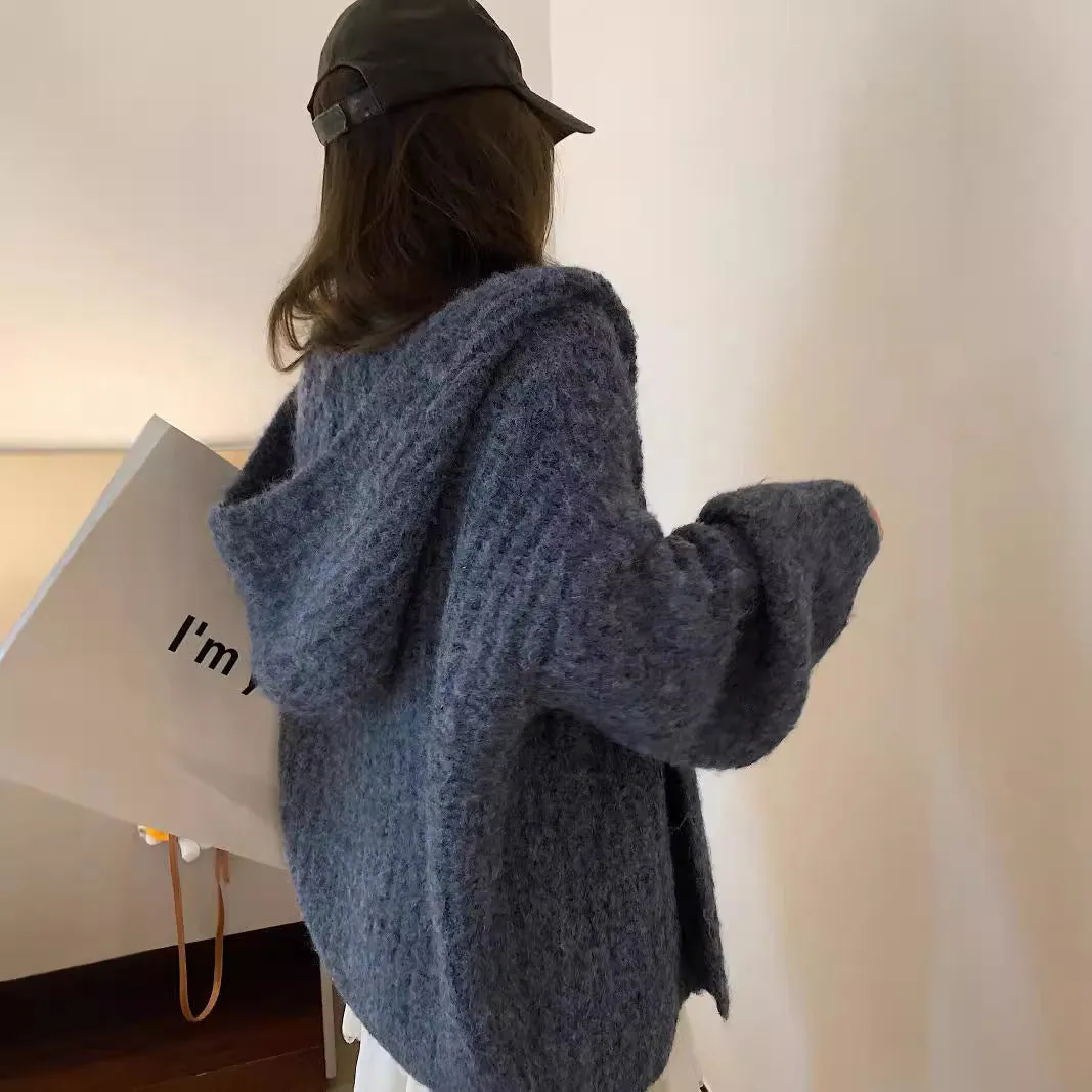 A woman wearing a thick, loose-fit, dark grey hooded sweater cardigan with a retro design.