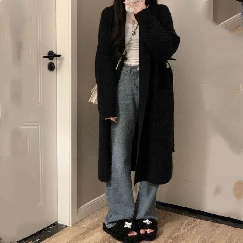 Loose large dark grey knitted cardigan with a 3D pattern, worn open over a top.