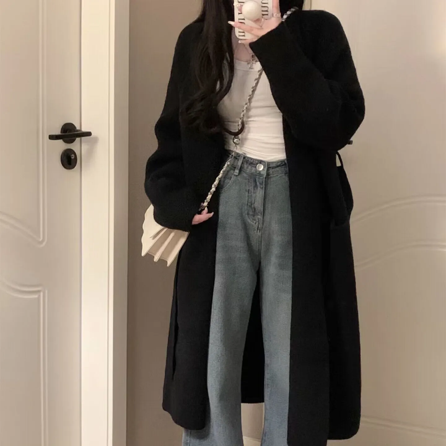Loose large dark grey knitted cardigan with a 3D pattern, worn open over a top.