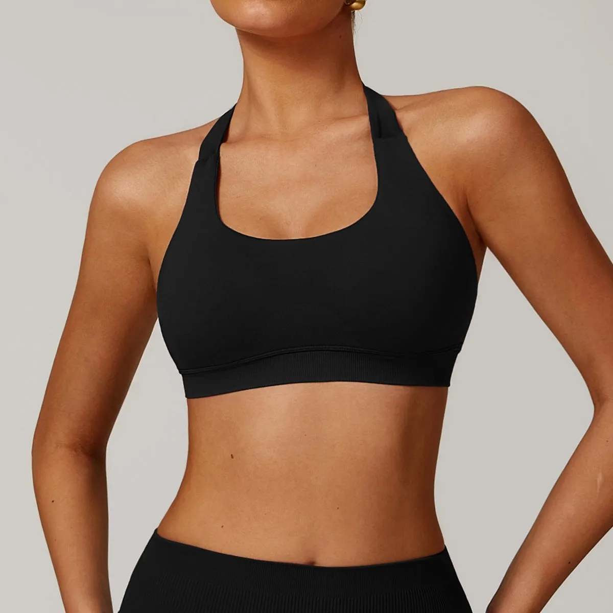 Women's black halter neck sports bra for yoga, shown from the front, with removable pads and a backless design.
