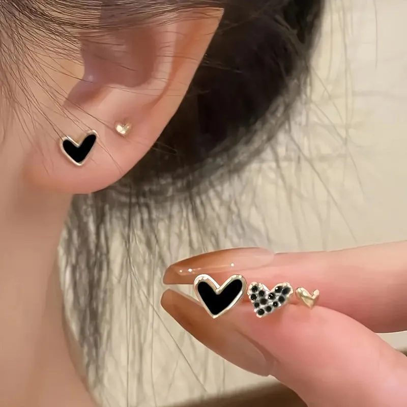 Set of three pairs of women's heart-shaped alloy earrings in gold, black, white, and pink.