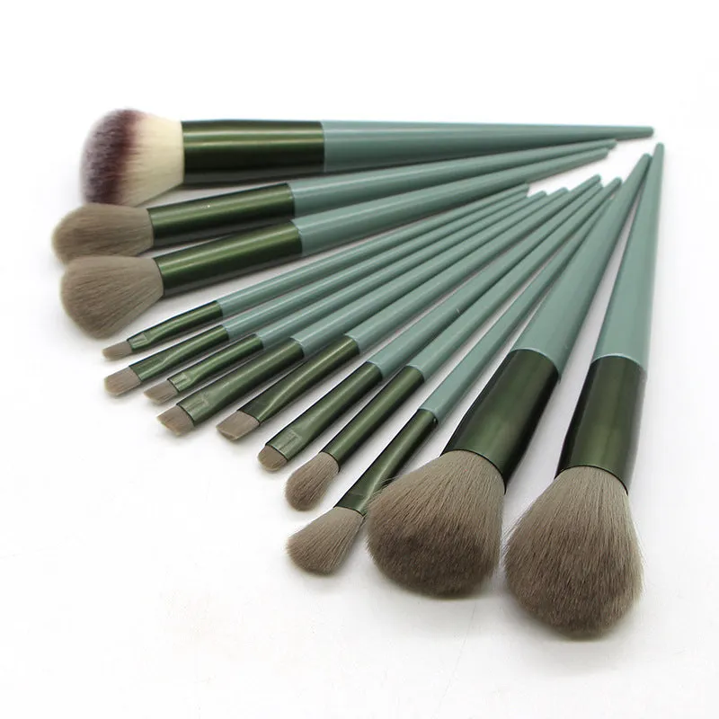13 green makeup brushes with fibre wool bristles and aluminium tubes arranged on a surface