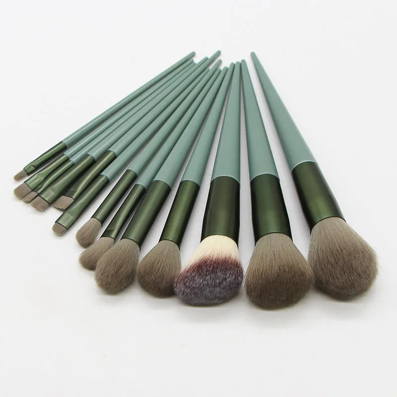 13 green makeup brushes with fibre wool bristles and aluminium tubes arranged on a surface