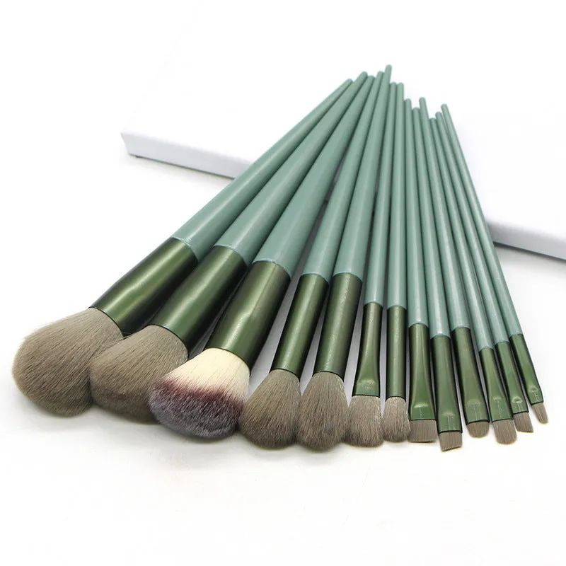 13 green makeup brushes with fibre wool bristles and aluminium tubes arranged on a surface