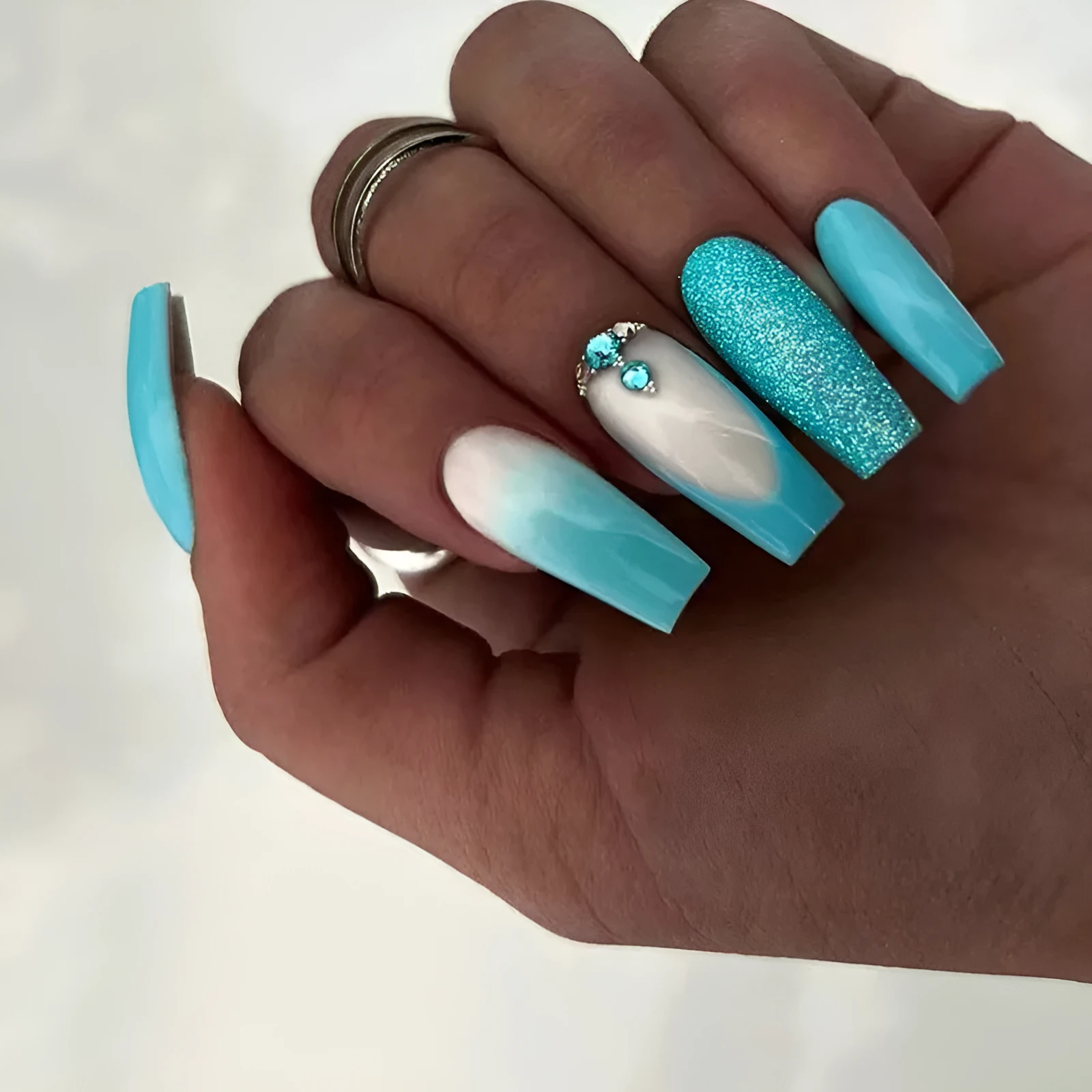 Long ballet shaped false nails in solid blue diamond colour with glitter adhesive glue.
