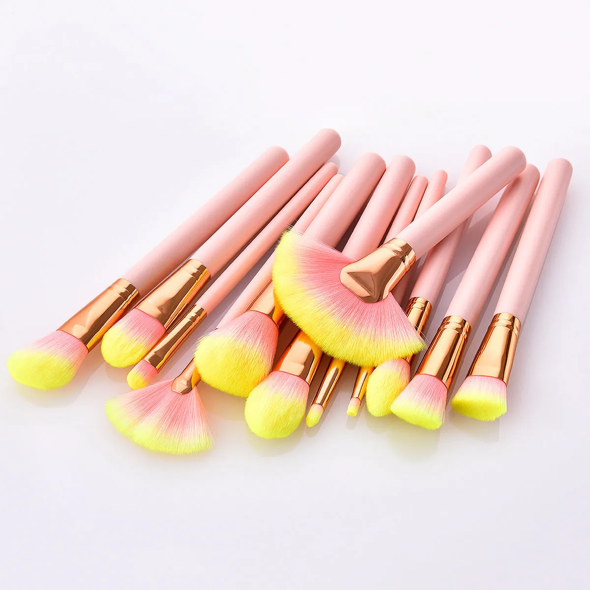 Twelve pink makeup brushes with nylon bristles and wood handles laid out in a row on a light background