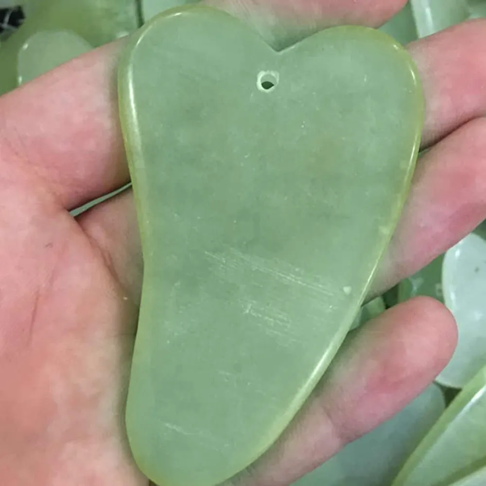 Natural green jade face massager roller and scraper set on a clean surface