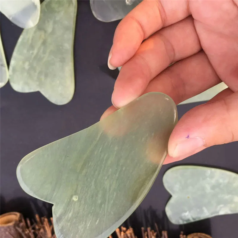 Natural jade gua sha scraper in heart shape on a light surface, 6.3cm x 4.5cm, hand-polished stone
