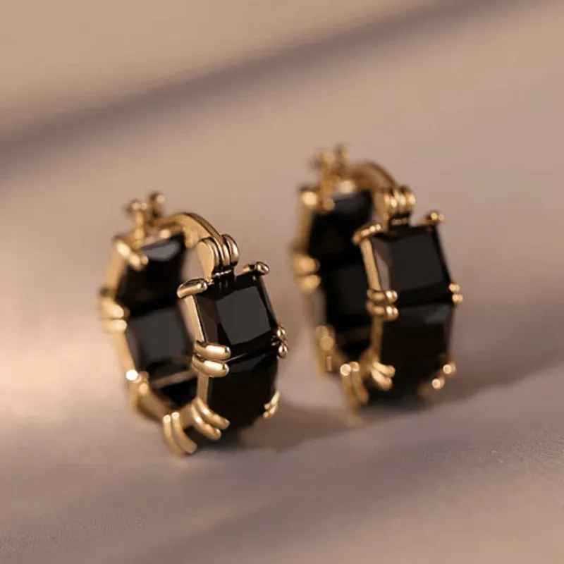 Women's geometric U-shaped gold earrings with round black zircon crystals on white background
