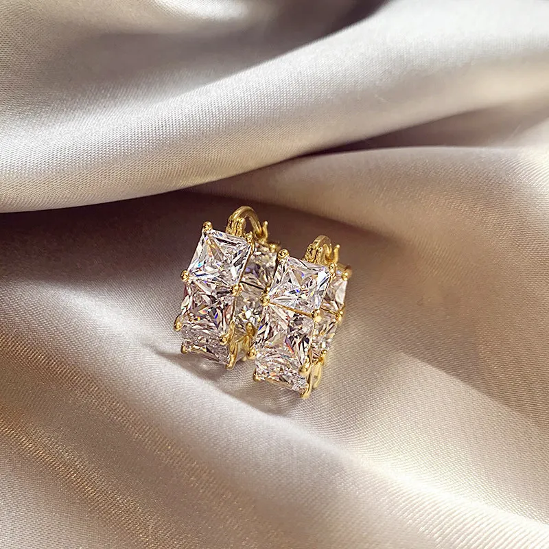 Women's geometric U-shaped gold earrings with round black zircon crystals on white background