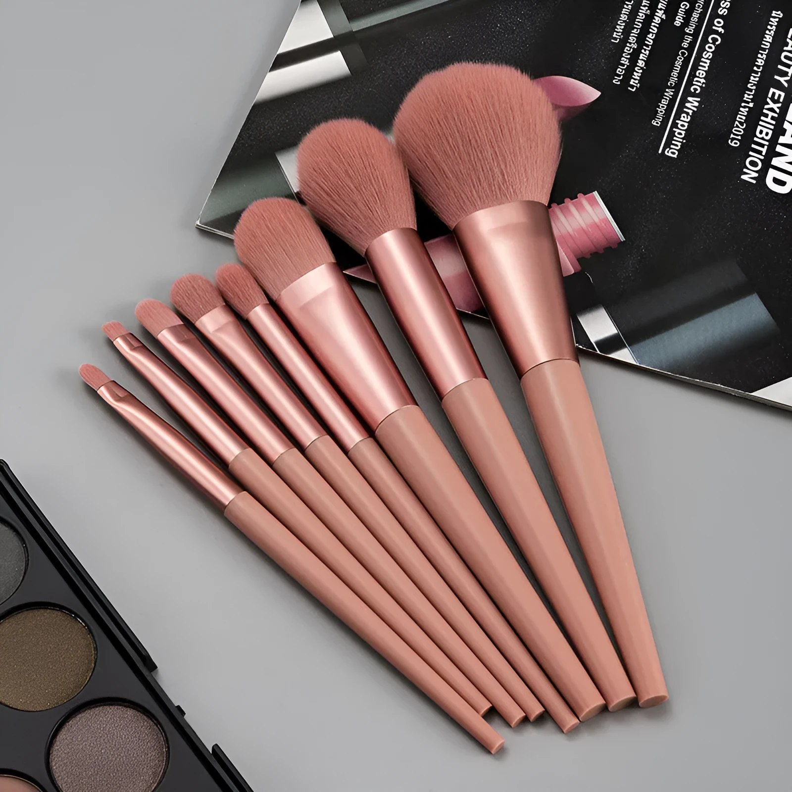 Pink 8-piece makeup brush set with man-made fibre bristles and plastic handles on a light background.