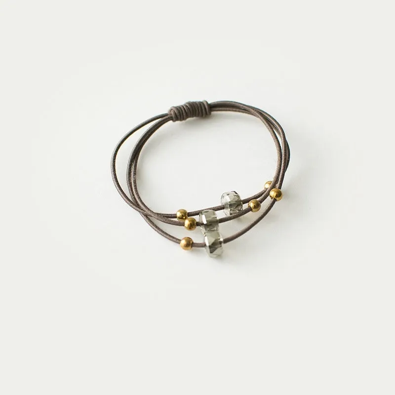 Crystal string beads rubber knotted hair band with octagonal electroplated beads in matte golden, on a plain background.