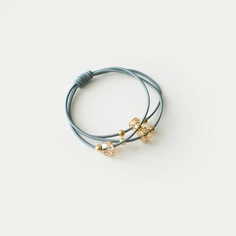 Crystal string beads rubber knotted hair band with octagonal electroplated beads in matte golden, on a plain background.