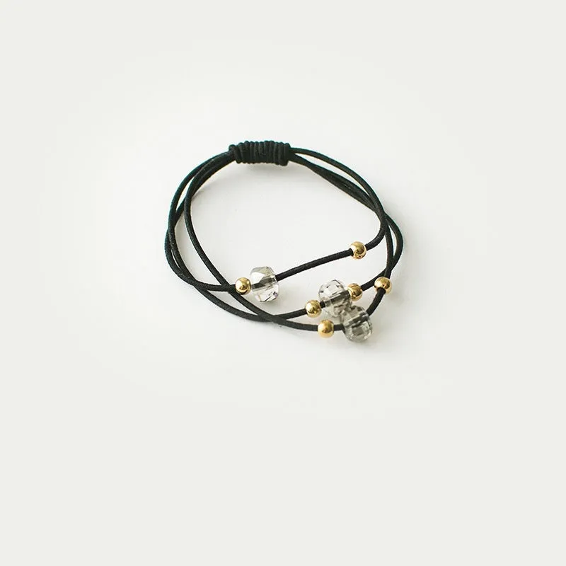 Crystal string beads rubber knotted hair band with octagonal electroplated beads in matte golden, on a plain background.