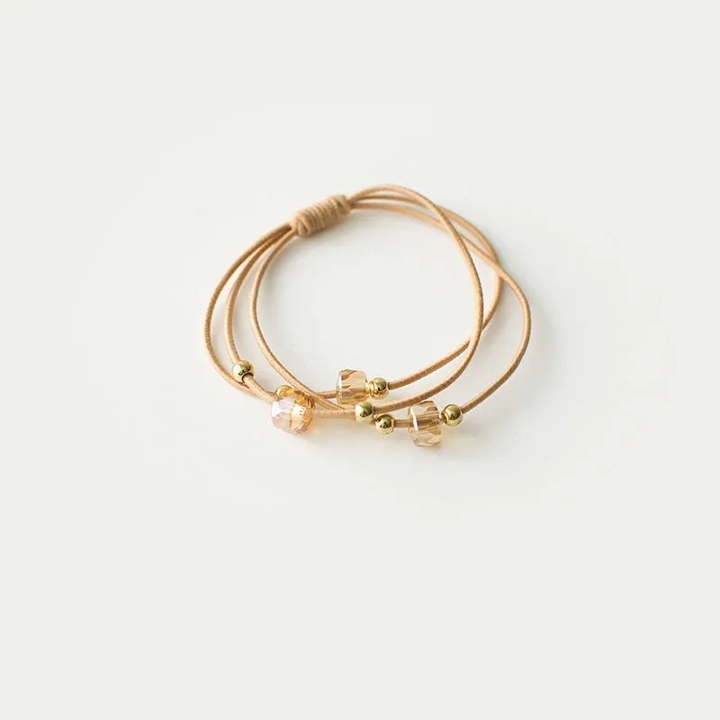 Crystal string beads rubber knotted hair band with octagonal electroplated beads in matte golden, on a plain background.