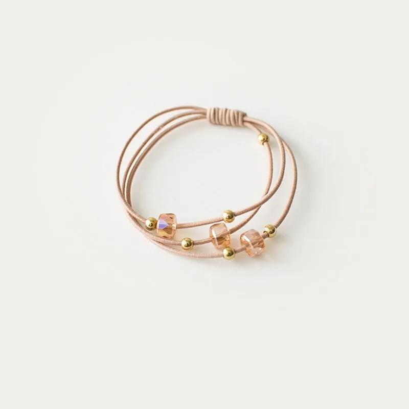 Crystal string beads rubber knotted hair band with octagonal electroplated beads in matte golden, on a plain background.