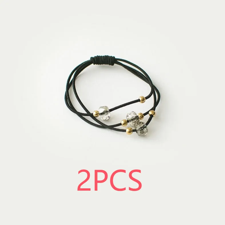 Crystal string beads rubber knotted hair band with octagonal electroplated beads in matte golden, on a plain background.