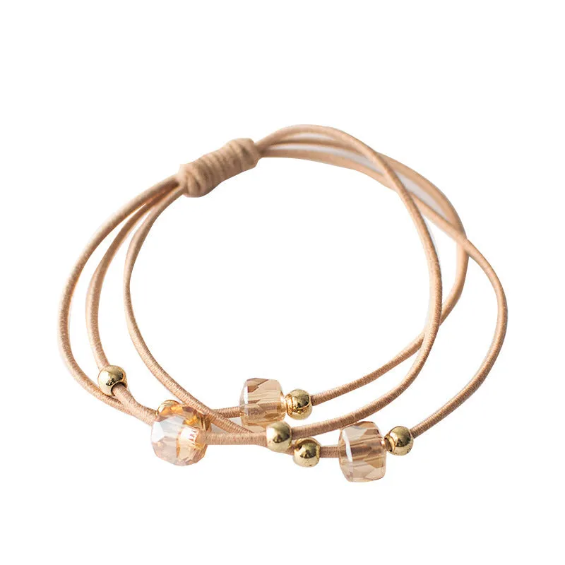 Crystal string beads rubber knotted hair band with octagonal electroplated beads in matte golden, on a plain background.