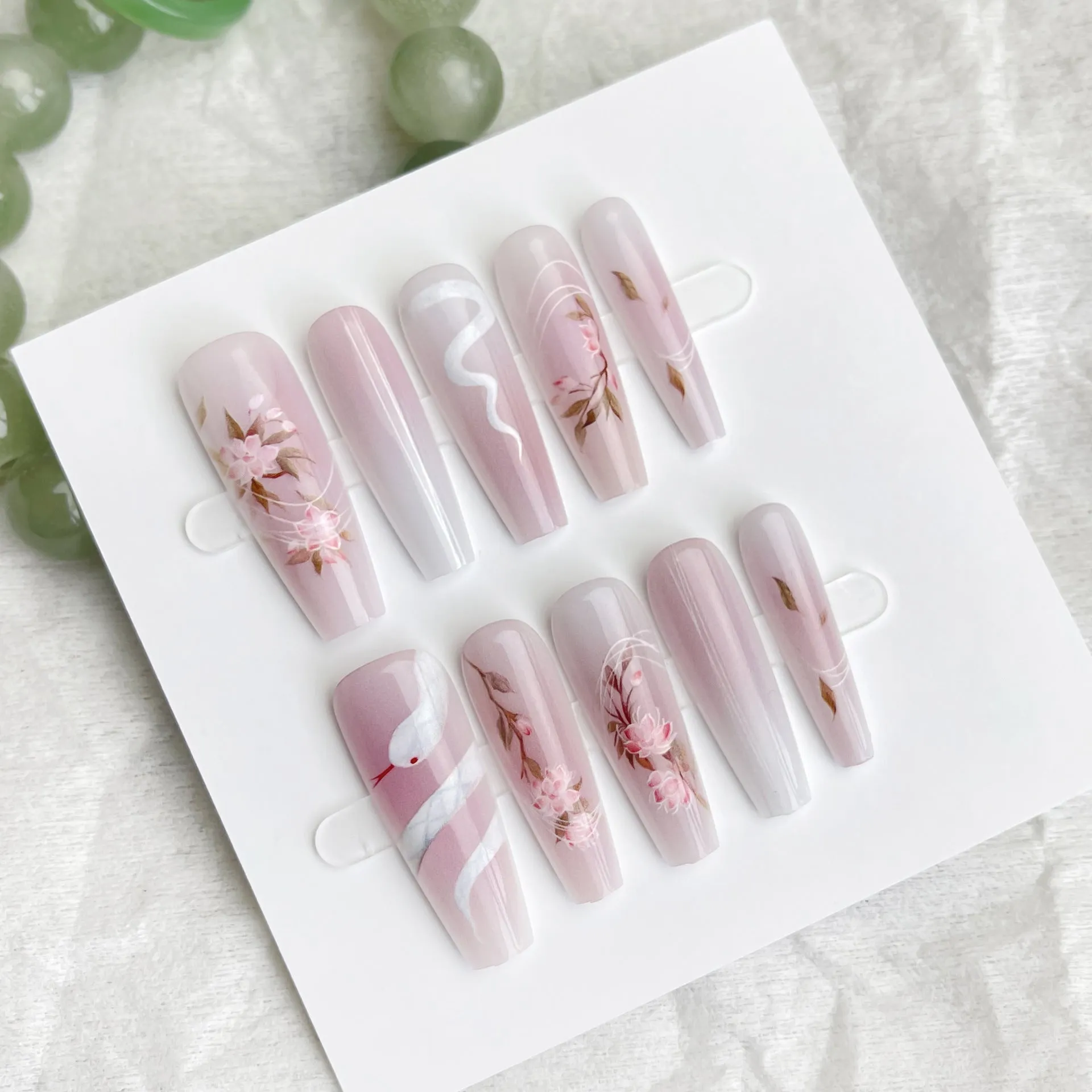 Ancient Chinese style snake year red prefabricated nail tips in drunk flower colour, long ladder shape, on a display stand