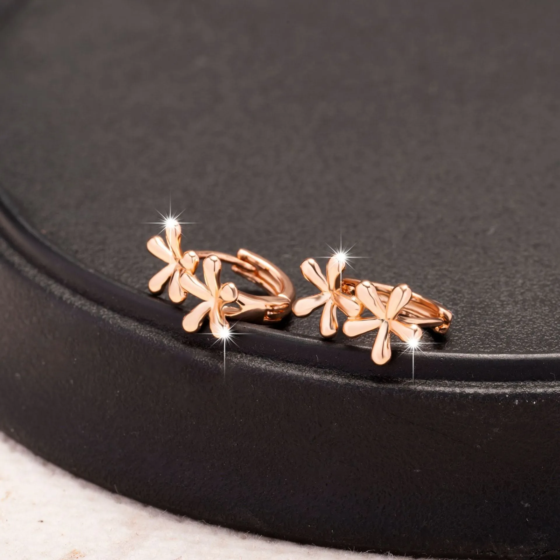 Rose gold circular earrings with a raised waterdrop floral design on a white background.