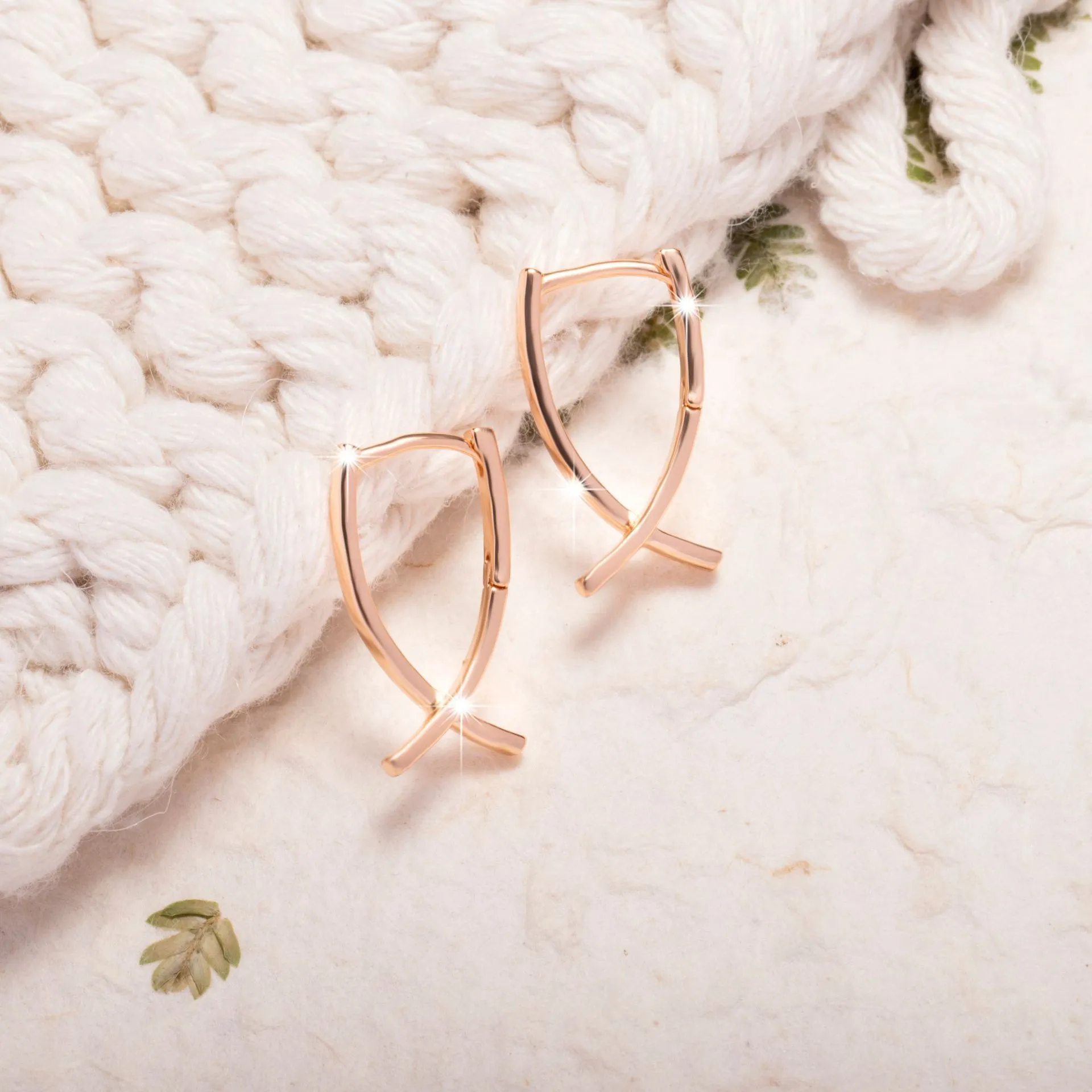 A pair of rose gold coloured cross shaped earrings made from copper on a plain background.