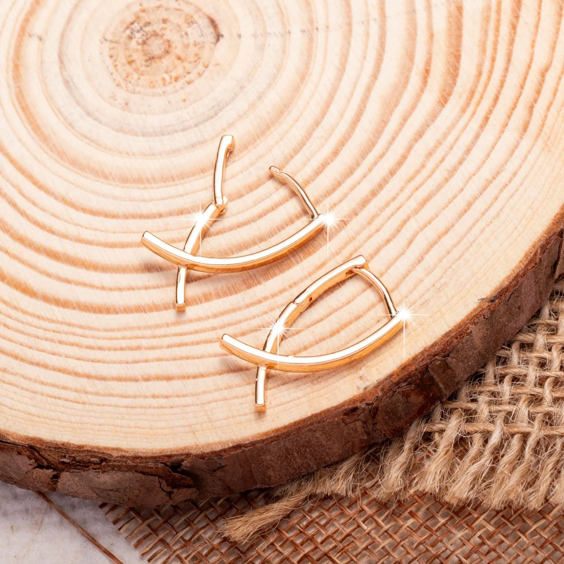 A pair of rose gold coloured cross shaped earrings made from copper on a plain background.